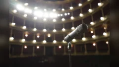 Close-up of a microphone on stage with bright theater lights in the background.